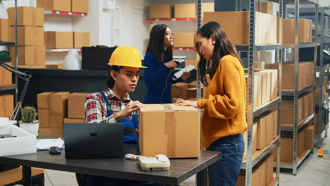 An order team checking stock and packing parcels in a warehouse, a laptop on the desk.